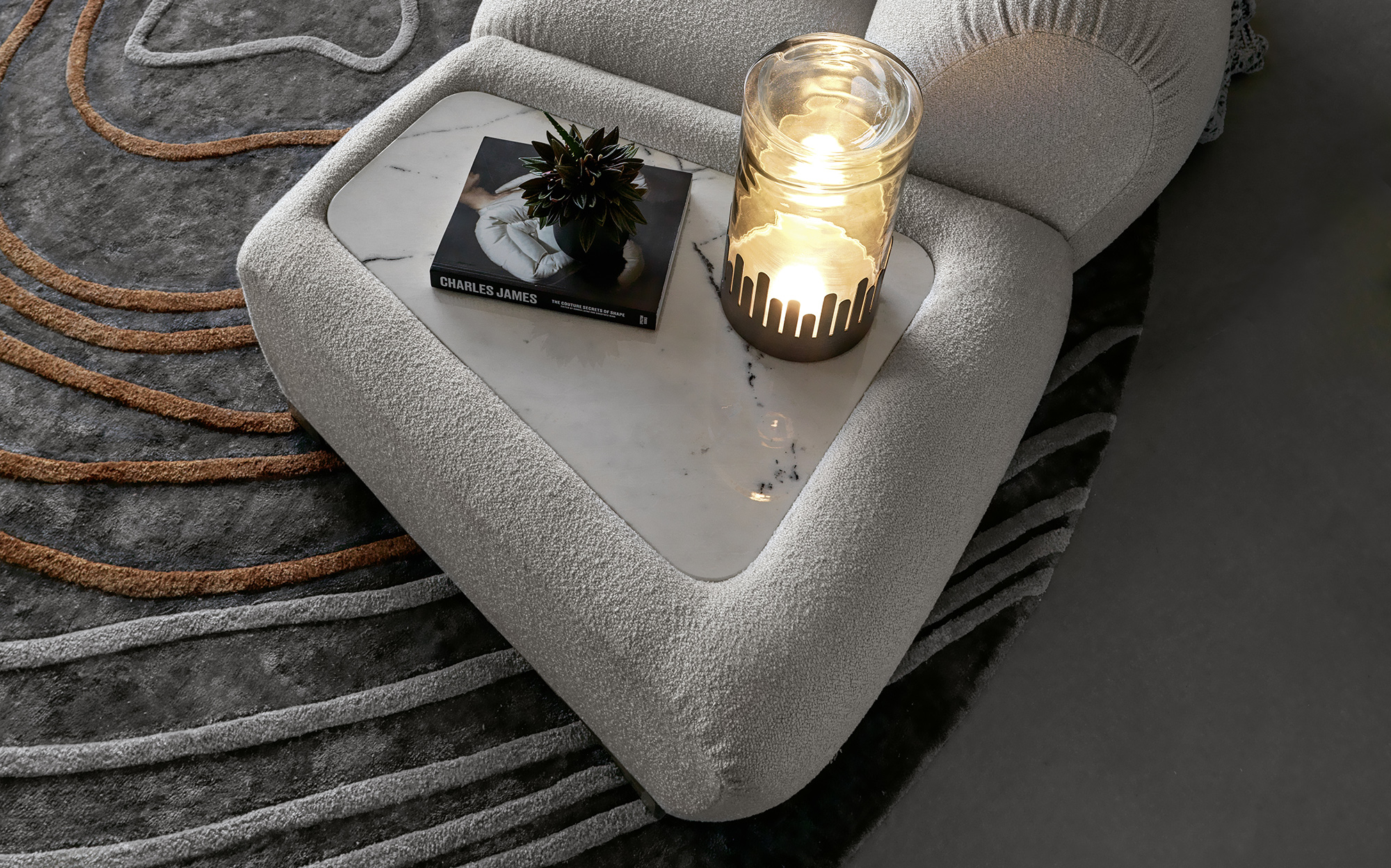 Refined corner with marble and soft light for luxury interiors | 101DOMUS Sofa detail with marble insert, decorative candle and design book