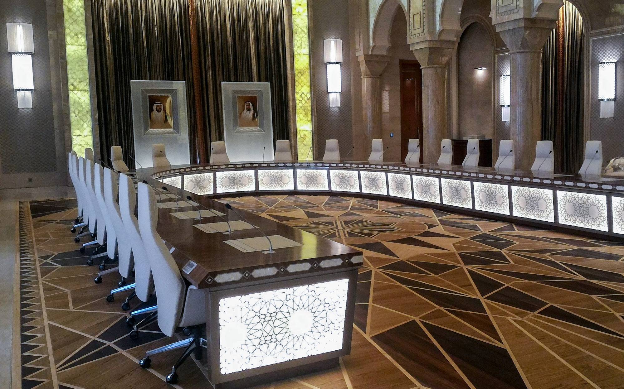 Long council table with inlaid front panels and white chairs under stone arches, Qasr Al Watan Abu Dhabi | 101domus