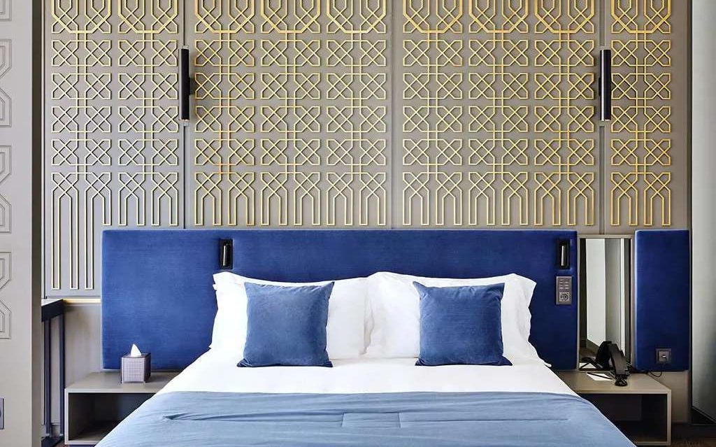 Bed with blue upholstered headboard against a gold lattice wall, Boutique Hotel Stresa by Francesco Molon | 101domus