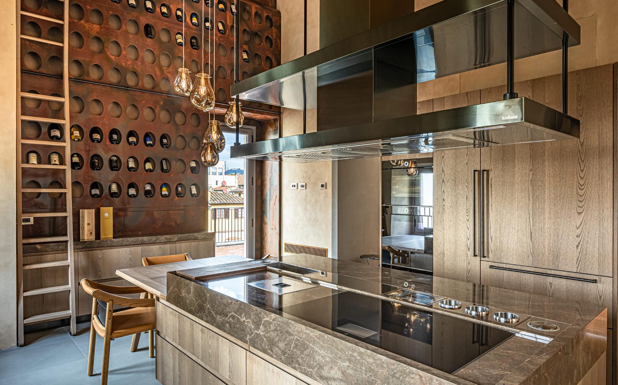 Apartment kitchen with stone island, steel hood and wine wall, Palazzo Portinari Salviati by Francesco Molon | 101domus